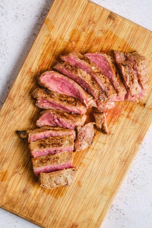 Juicy seared surf and turf steak sliced on wooden cutting board, grilled to medium rare.