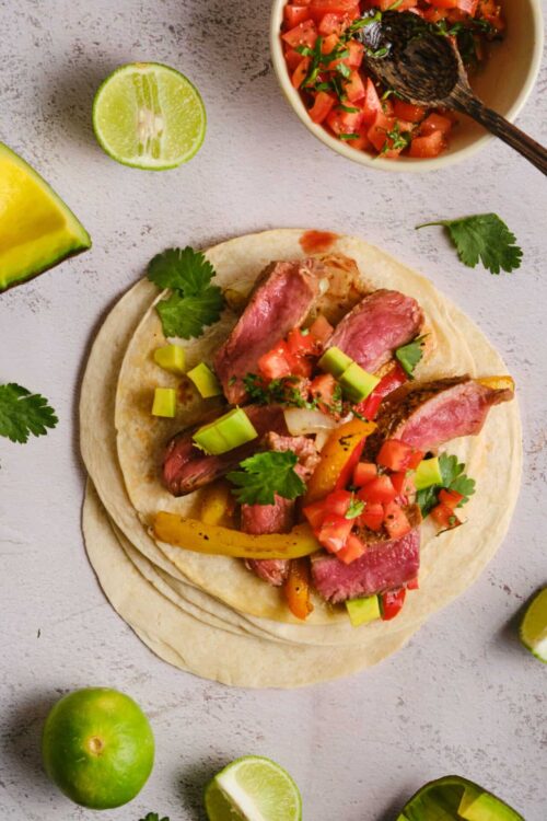 Sliced steak and colorful peppers on a soft flour tortilla for steak fajitas recipe.