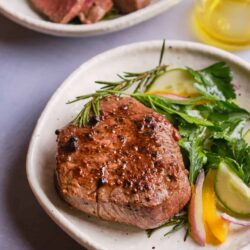 Juicy grilled steak with fresh herbs and colorful salad on a rustic plate.