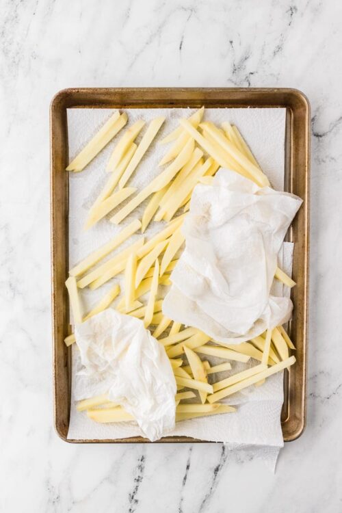 Raw cheese slices on parchment paper in a baking tray for cheese sticks recipe.
