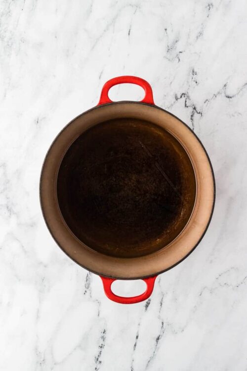 Heavy-bottomed cast iron skillet with a red handle on a white marble surface.