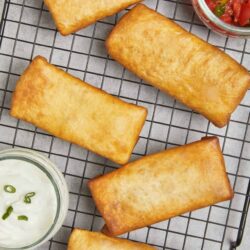 Golden fried fish fillets on a cooling rack with side sauces.