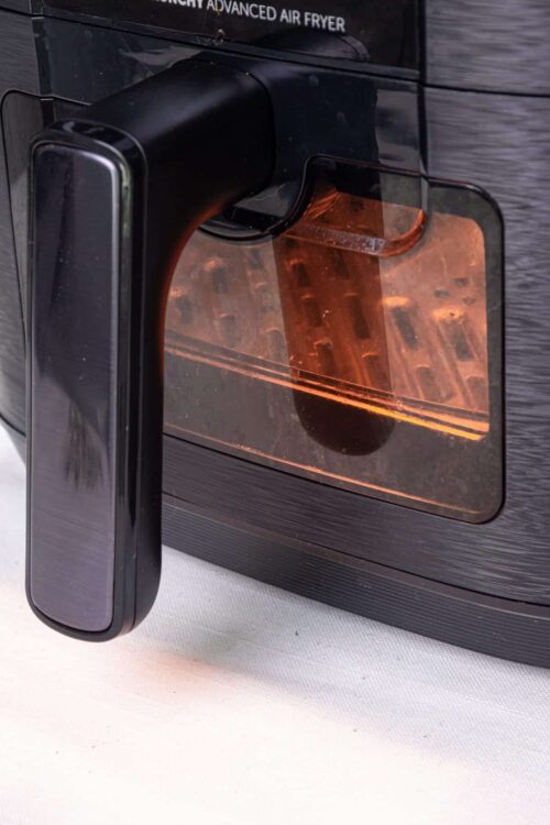 Hot air fryer cooking food, modern kitchen appliance, black air fryer with transparent door, countertop kitchen gadget.