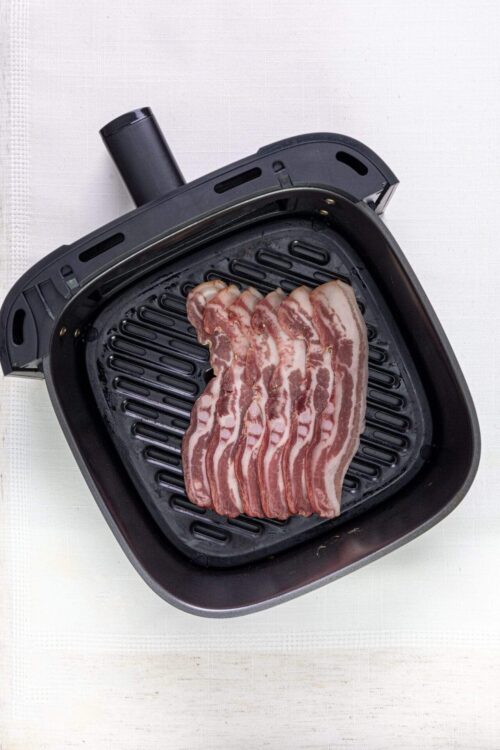 Raw bacon slices cooking in an electric indoor grill for breakfast or brunch.