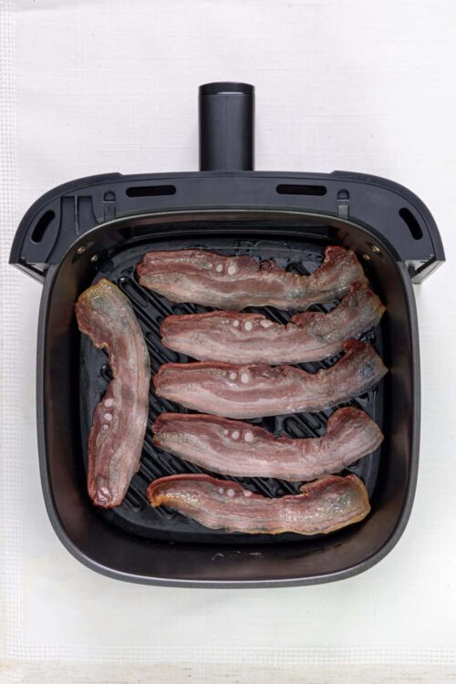 Sliced bacon cooking in an electric skillet.
