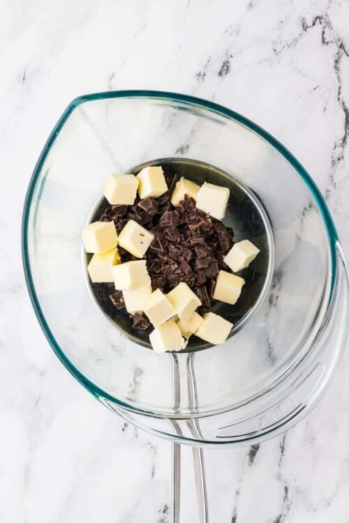 Chopped white and dark chocolate in glass mixing bowls on white marble surface.