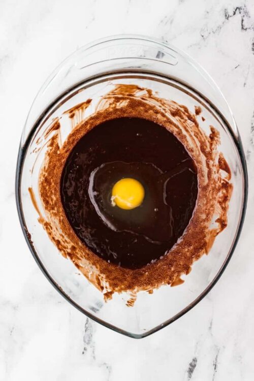 Rich chocolate batter with a raw egg in a glass mixing bowl for baking or dessert preparation.