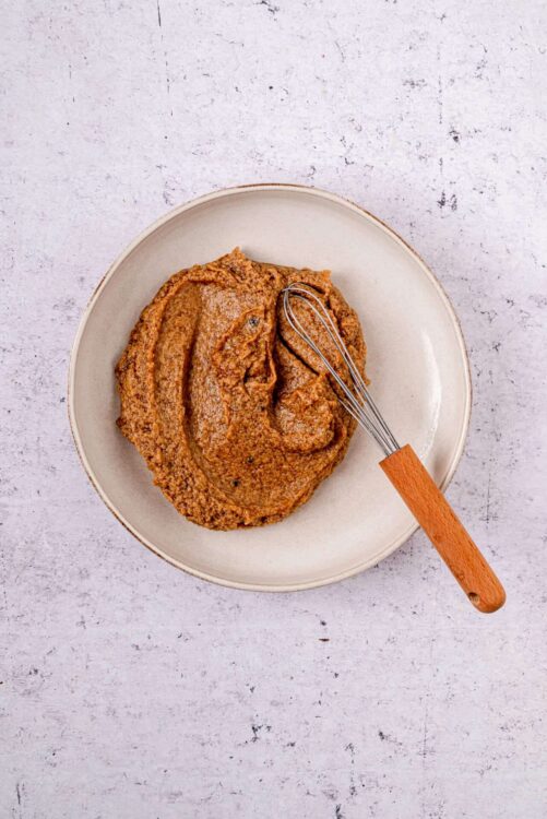 Creamy peanut butter on a beige plate with a small whisk, perfect for homemade peanut butter recipes and spreads.