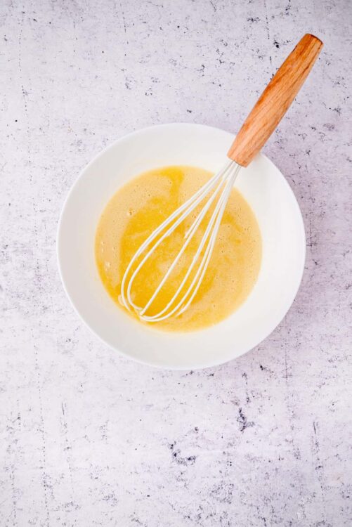 Smooth vanilla cake batter with a whisk in white bowl on rustic background.