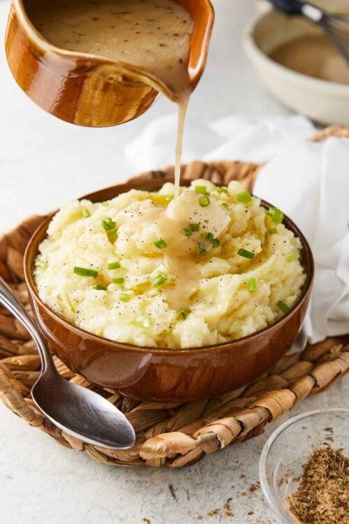 Creamy mashed potatoes with gravy served in a brown bowl, topped with chopped green onions.