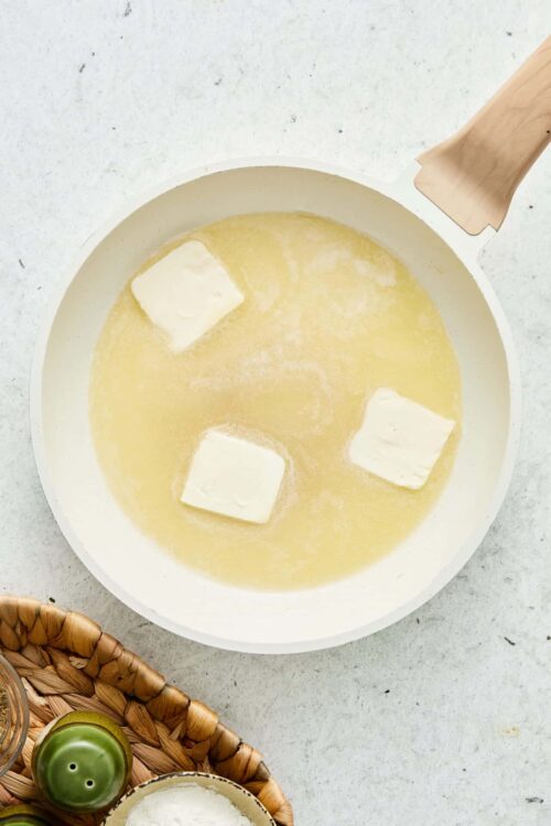 Butter melting in a white skillet over low heat over light gray countertop.