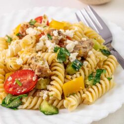 Creamy pasta salad with rotini, cherry tomatoes, cucumbers, yellow peppers, and crumbled feta cheese.