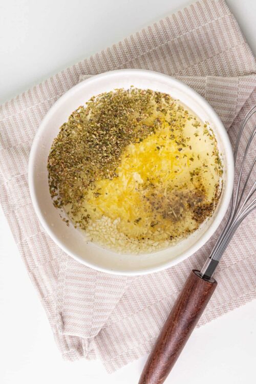 Fresh herbs in a bowl of marinade or seasoning mixture with whisks.