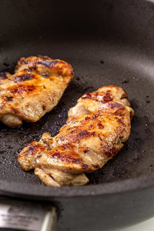 Juicy, golden-brown chicken breasts cooking in a black skillet, perfect for delicious baked chicken recipes.