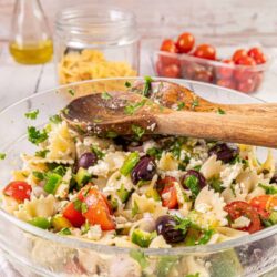 Fresh vegetable pasta salad with cherry tomatoes, olives, feta, and herbs in a glass bowl.