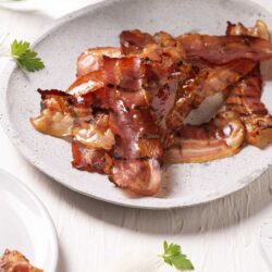 Crispy baked bacon strips on a speckled ceramic plate.
