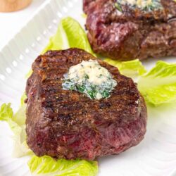 Juicy beef steaks with herb butter on lettuce leaf on white plate.
