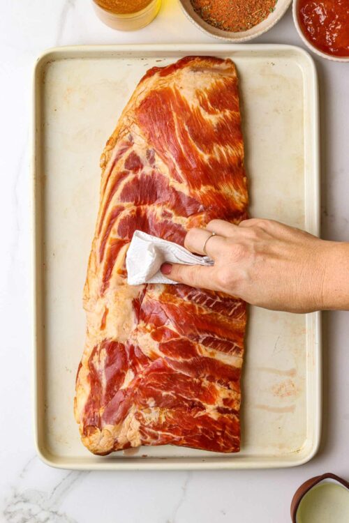 Juicy pork belly being seasoned with a paper towel for roasting.