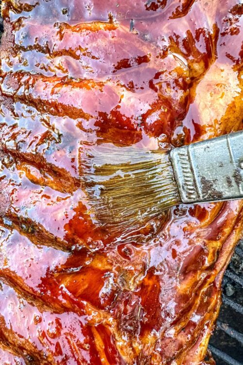 Succulent pork ribs being coated with barbecue sauce with a basting brush.