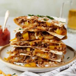 Hearty beef and cheese quesadillas with colorful peppers on a white plate, served with side dishes.
