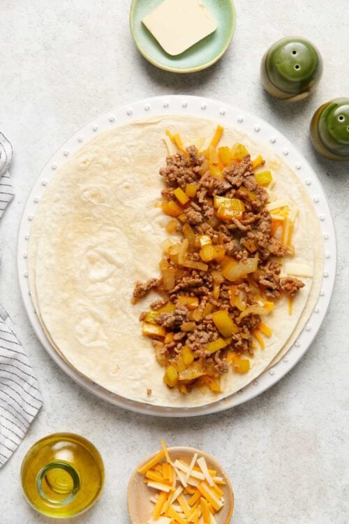 Ground beef and cheese filling for homemade burritos on a large white plate, ready to roll.