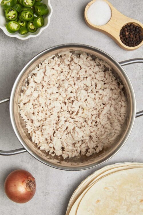 Minced cooked chicken in a stainless steel skillet for recipe preparation.