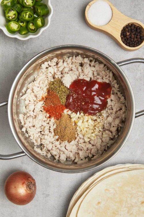 Minced chicken with spices, ketchup, and garlic in a metal bowl for homemade tacos or burritos.