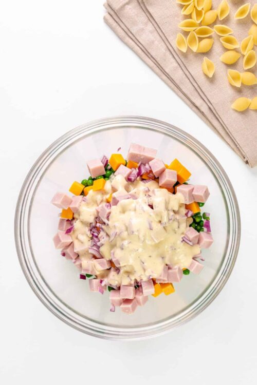 Diced ham, cheese, peas, and onions in a creamy salad dressing in a glass bowl.