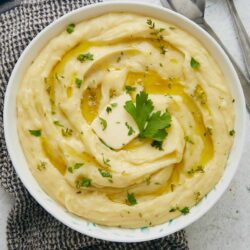 Creamy mashed potatoes with garlic and herbs topped with olive oil and fresh parsley.