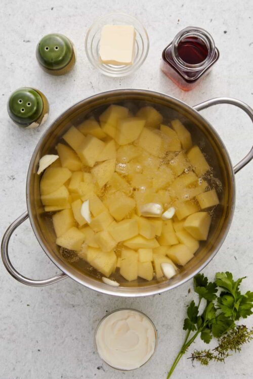 Creamy mashed potatoes cooking in a pot with herbs and garlic.