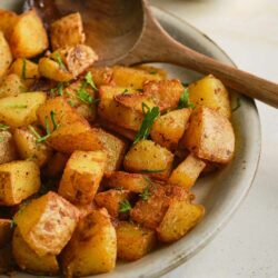Crispy roasted potatoes with herbs on a ceramic plate, served with a wooden spoon. Perfect for breakfast or side dishes.