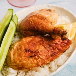 Juicy roasted chicken thigh and breast with rice and cucumber slices on a white dish.