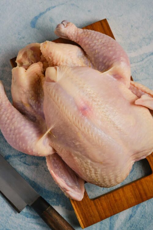 Raw whole chicken on a cutting board, ready for cooking or roasting.