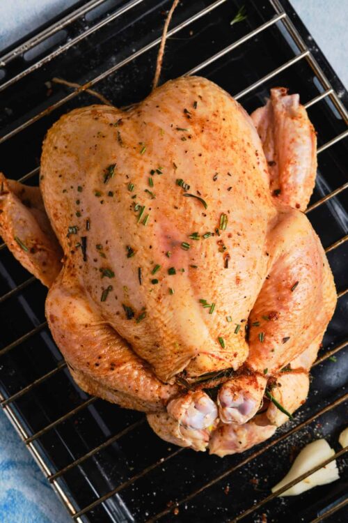 Juicy roasted whole chicken seasoned with herbs on a baking rack.