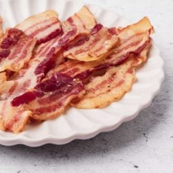 Crispy bacon strips on a white scalloped-edge plate, perfect for breakfast or brunch.