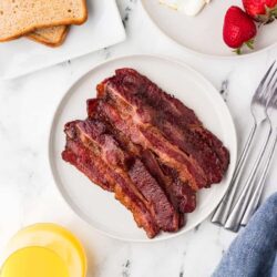 Baked Bree breakfast with crispy bacon, sunny side up eggs, strawberries, and toasted bread on white marble background.