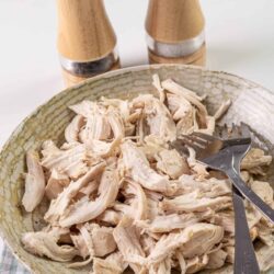 Shredded cooked chicken in a decorative bowl with salt and pepper shakers in the background.