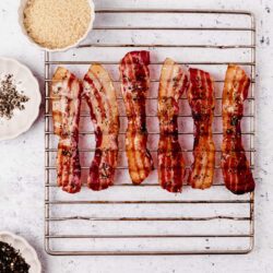 Crispy bacon strips seasoned with black pepper on a wire rack.