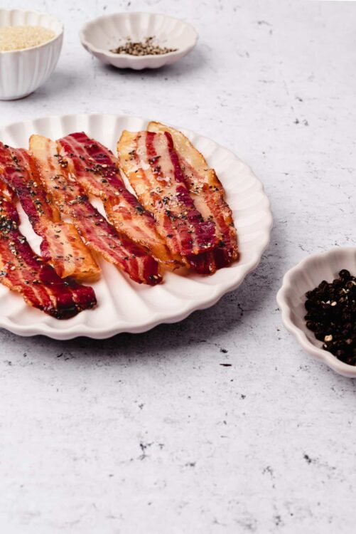 Crispy bacon strips sprinkled with black pepper on a white plate.