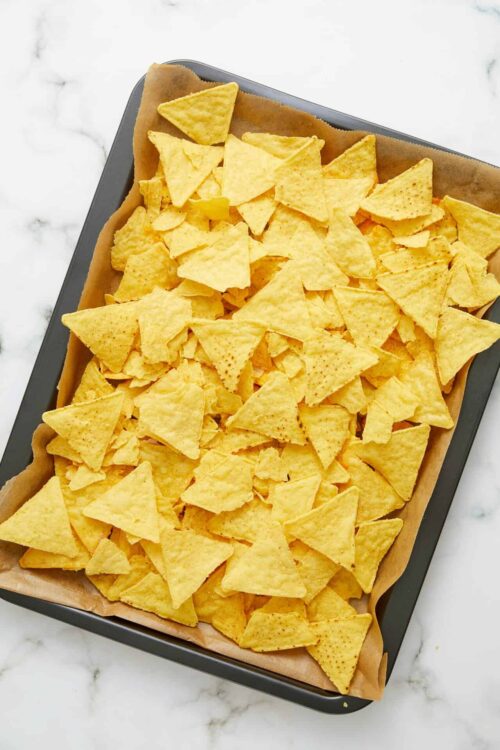 Golden baked tortilla chips on baking sheet, ready for snacks or dips.