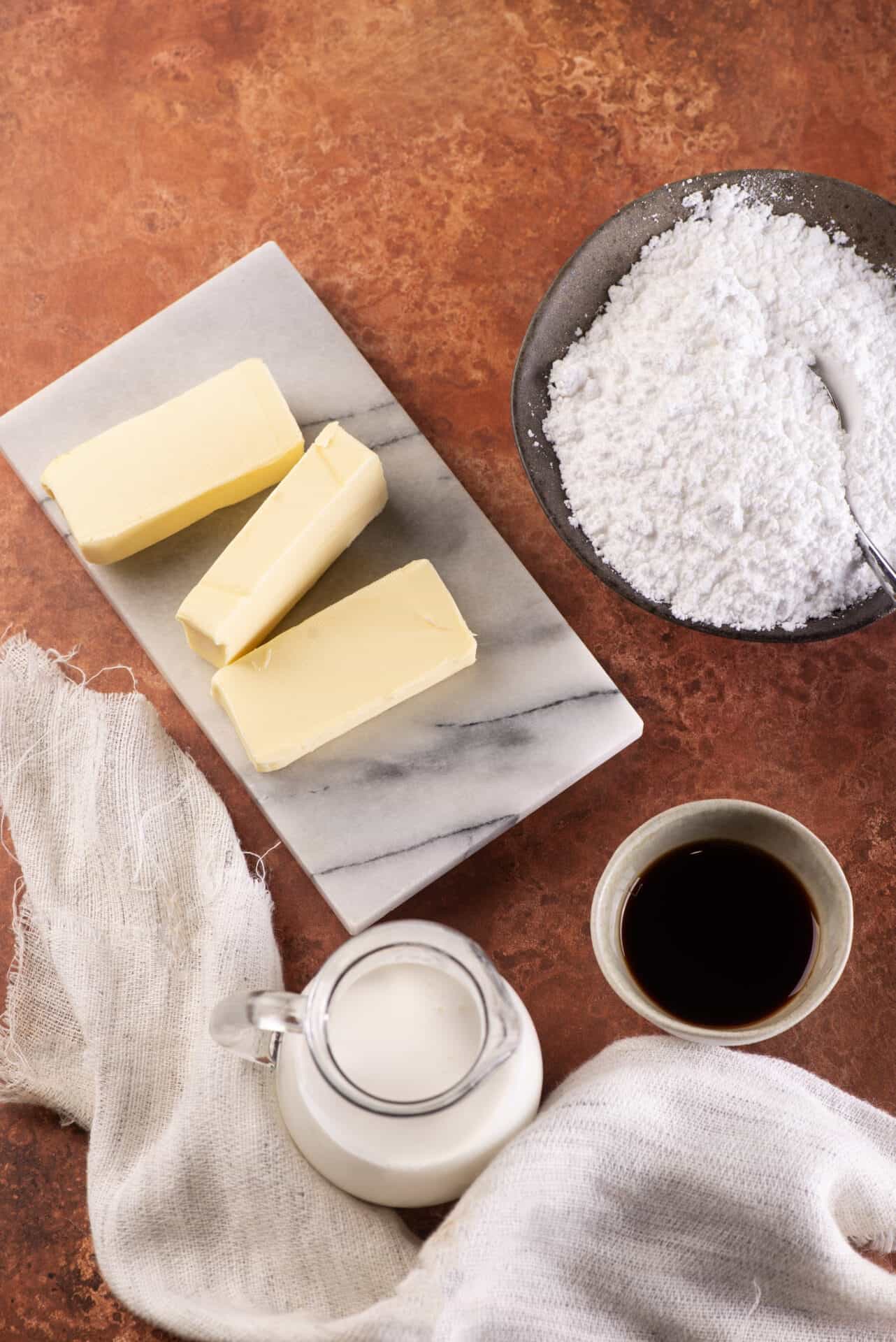 Butter and flour for baking on a marble tray and dark textured surface, with a cup of coffee and milk pitcher, baking ingredients, baking essentials, dessert making, culinary preparation.