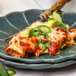 Crispy chicken enchiladas with melted cheese, avocado, and jalapenos on a dark green plate.