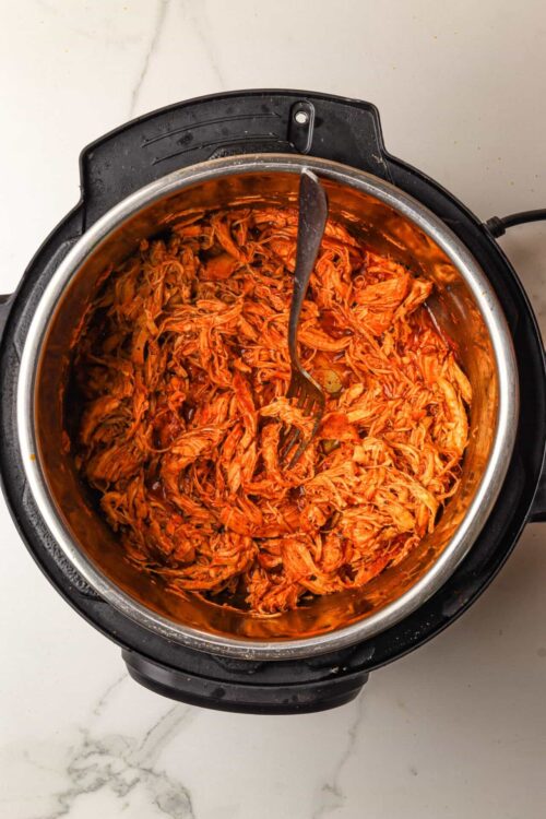Shredded cooked chicken in a slow cooker with barbecue sauce, ready for serving or further recipe steps.