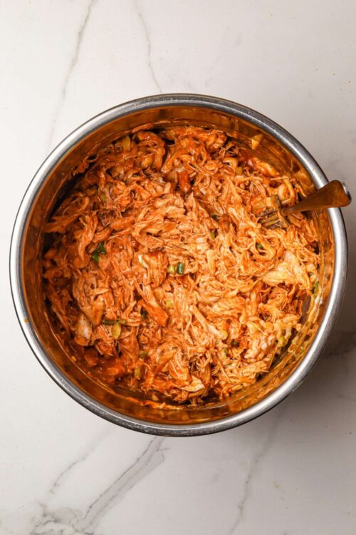 Shredded chicken in rich, flavorful barbecue sauce in a stainless steel mixing bowl.