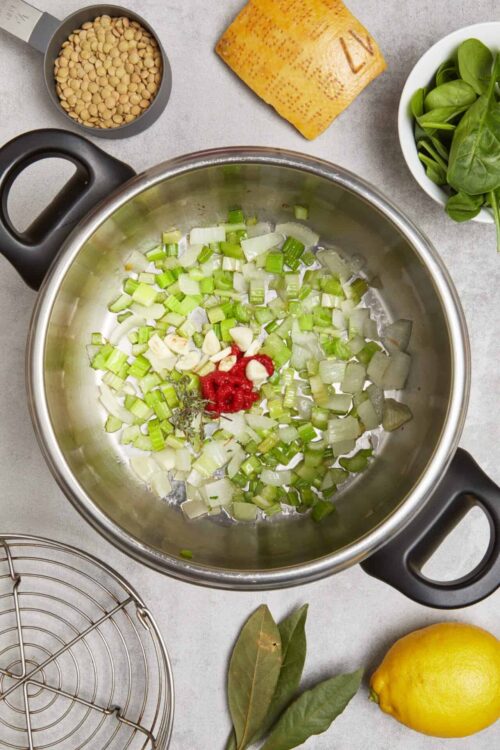 Chopped celery, garlic, and herbs sautéing in a stainless steel pot for cooking.