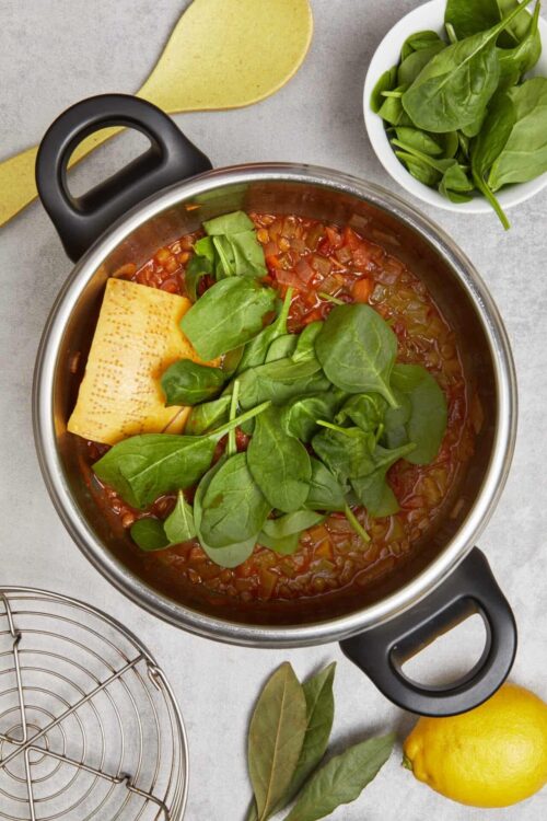 Fresh vegetable soup topped with spinach and cheese in a stainless steel pot.