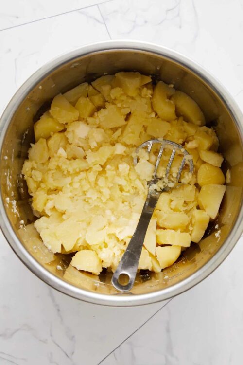 Creamed potatoes in a saucepan with a metal masher.
