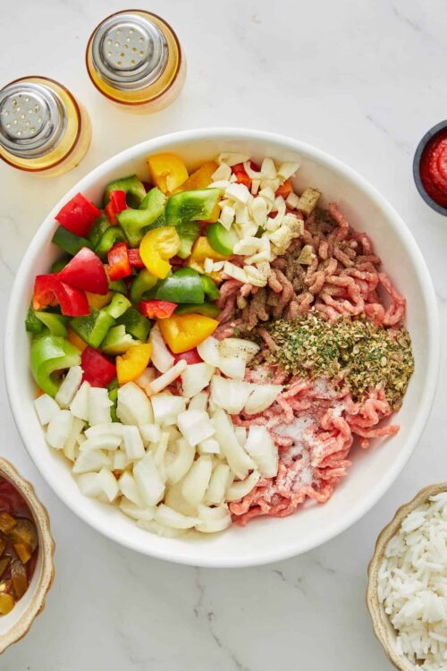 Chopped colorful bell peppers, onions, ground beef, and seasonings in a mixing bowl for a keto or healthy ground meat recipe.