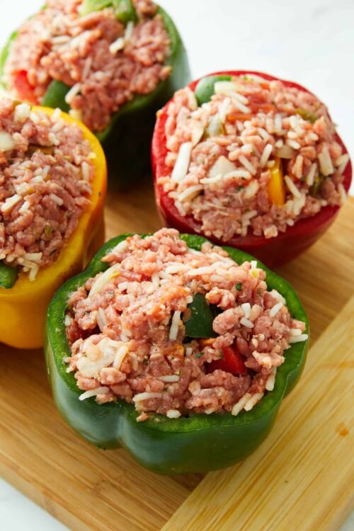 Stuffed bell peppers filled with seasoned ground meat and shredded cheese, arranged on a wooden cutting board.