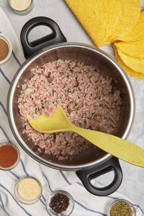 Ground beef in a stainless steel pot for taco filling preparation.
